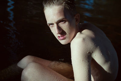 Portrait of young shirtless man lying sitting in lake