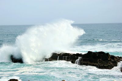 Waves splashing on sea against clear sky