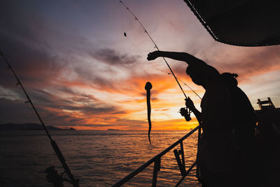 Silhouette young man fishing in open sea from the boat