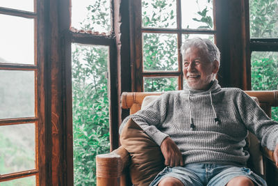 Smiling senior man sitting on chair by window