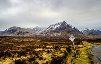 Road sign on field against cloudy sky