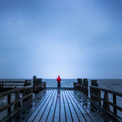 Rear view of man standing on pier over sea against blue sky