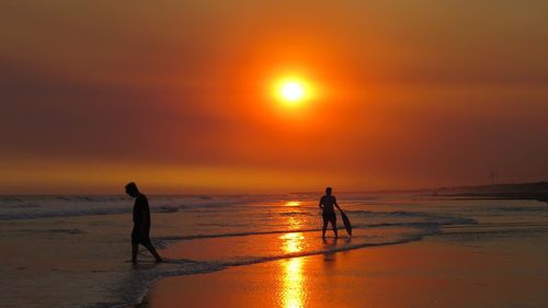 Silhouette people on beach against sky during sunset