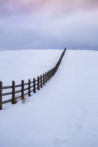 Wooden posts on snow covered land against sky