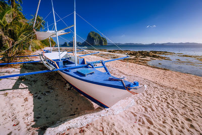 Sailboats moored on beach against blue sky