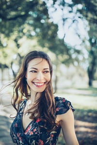 Portrait of cheerful optimistic brunette in a flower dress in the park, smiling. close up.