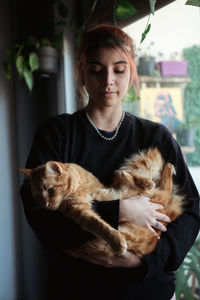 Woman holding cat standing at home