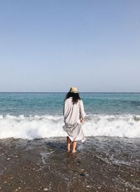 Rear view of woman standing at shore against clear sky