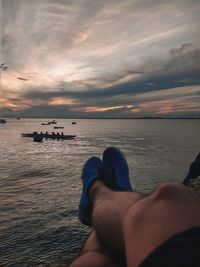 Low section of man on sea against sky during sunset