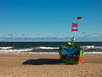 Boat moored on shore at beach against blue sky during sunny day