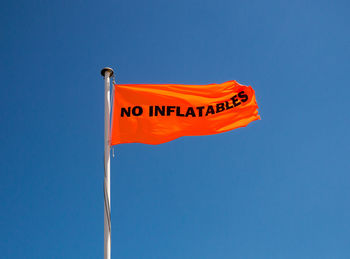 Low angle shot of an orange no inflatables flag on a grey metal pole against a clear blue sky