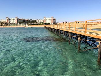 Bridge over sea by buildings against clear blue sky