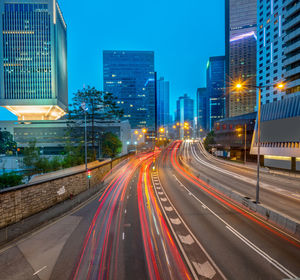 Light trails on road amidst buildings against sky at night