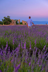 Rear view of woman walking on field by flowering plants against sky