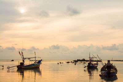 Fishing boats in sea against sky during sunset