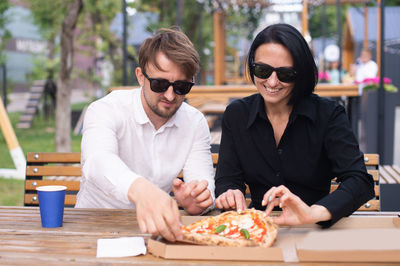 A married couple in a street restaurant drinking coffee and eating pizza