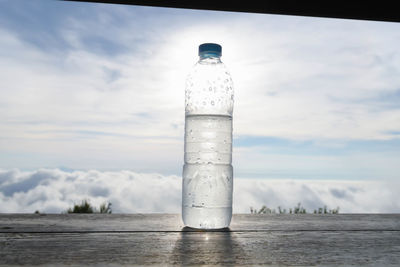 Cold water bottle on wooden table against cloudy sky