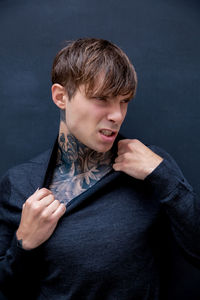 Angry young man with tattooed chest against black background
