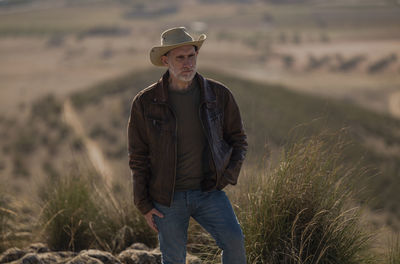 Portrait of adult man with cowboy hat standing on top of hill