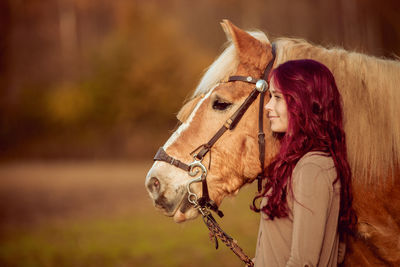 Red haired rider and brown horse next to each other look to side on orange pasture field