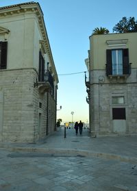 People walking on street amidst buildings in city against sky