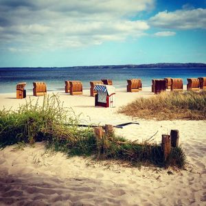 Hooded chairs on beach against sky