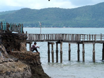 Man standing on rock by sea against sky