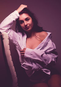 Portrait of sensuous woman in shirt sitting on chair against window