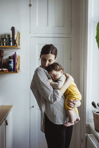 Mother carrying baby boy while standing at home