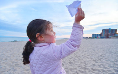 Cute young girl is playing with paper airplanes on the beach