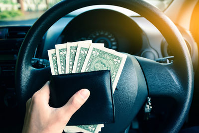 Cropped hand holding paper currencies in car