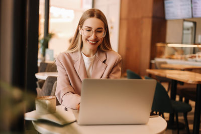 Portrait of a business woman student wearing headphones drinking coffee while working using a laptop