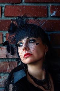 Thoughtful woman in widow hat looking away against brick wall