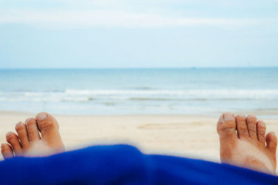 Low section of boy on beach against sky