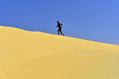 Man on sand dune in desert against clear blue sky