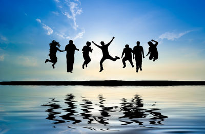 Silhouette people jumping in lake against sky during sunset