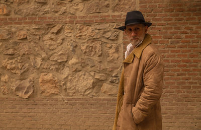 Portrait of adult man in hat and coat against brick wall on street. madrid, spain