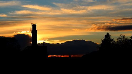 Silhouette factory against sky during sunset