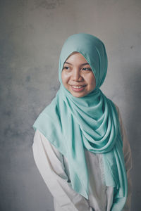 Smiling young woman wearing hijab while standing against wall