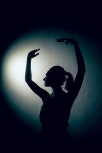 Silhouette woman with arms raised against black background