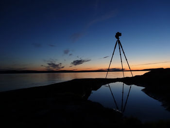 Low angle view of silhouette camera on tripod reflection in water at riverbank