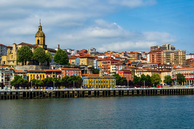 Buildings by river against cloudy sky