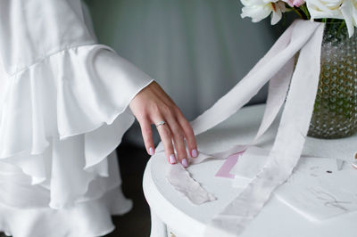 The bride runs her hand over the table on which  and pink ribbons from the bouquet are lying