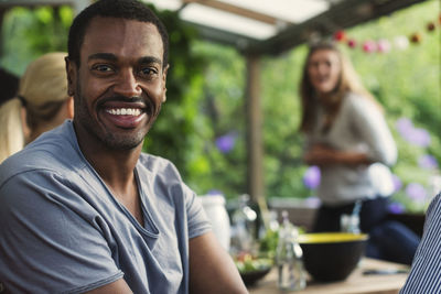 Portrait of happy man sitting with friends at porch in summer house