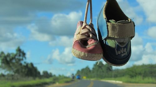 Close-up of baby shoes hanging on car windshield against sky