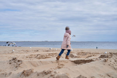 Cute girl fooling around at the beach in a winter coat