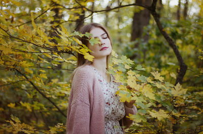 Woman standing by leaves against tree