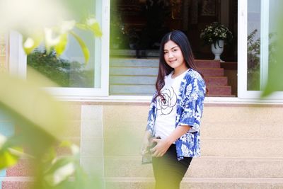 Portrait of smiling young woman standing by window