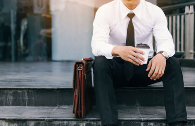 Midsection of businessman holding disposable coffee cup while sitting on staircase