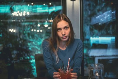 Portrait of young woman with drink sitting in restaurant